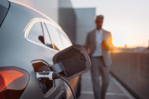 Close,Up,Of,Electric,Car,Charging,,Businessman,Standing,In,Background